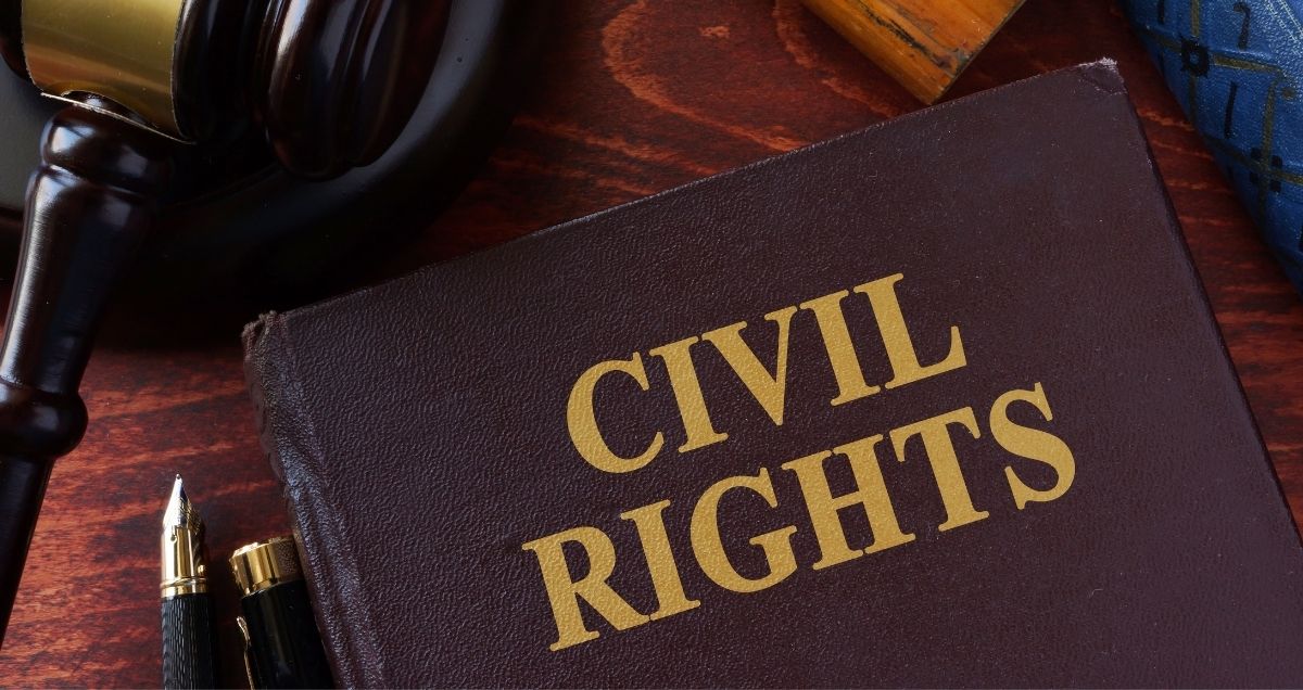 A civil rights book, gavel, and pen on a dark-wood desk.