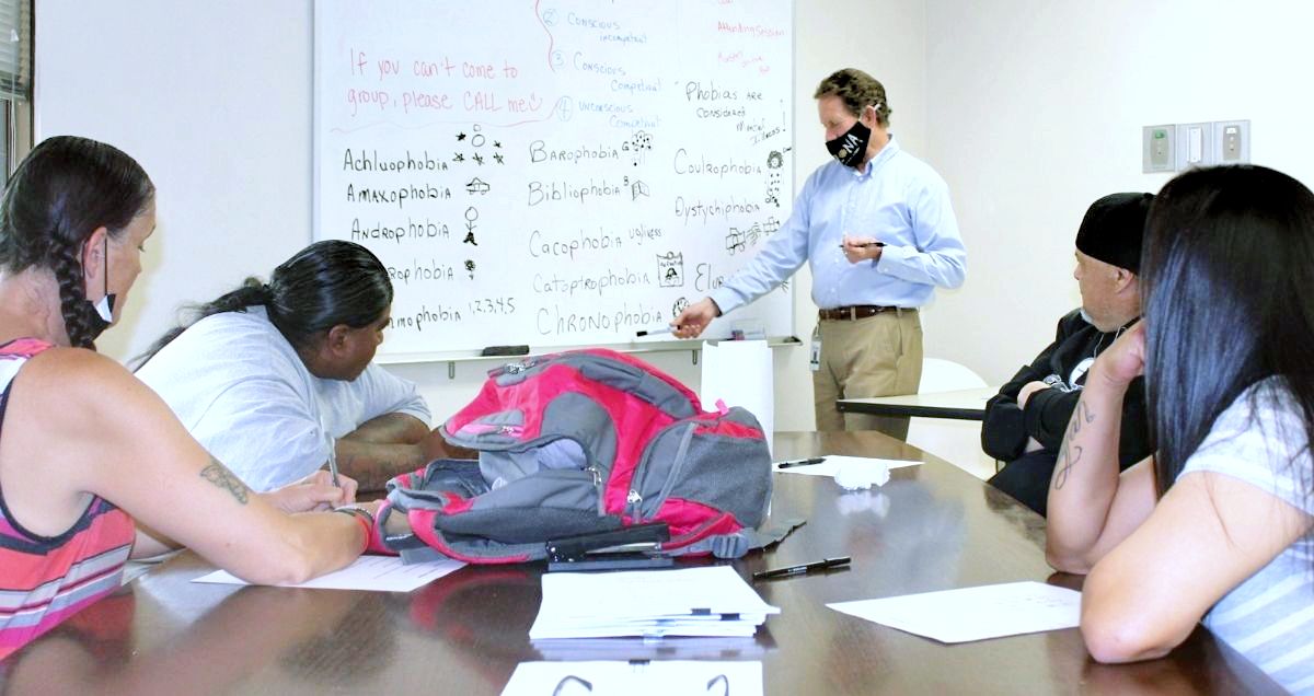 A group of people in a substance abuse recovery class learning from a teacher presenting at a dry erase board.