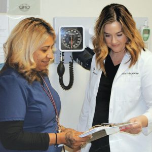 A nurse in scrubs and a doctor in a lab coat looking at a clipboard surrounded by medical equipment.