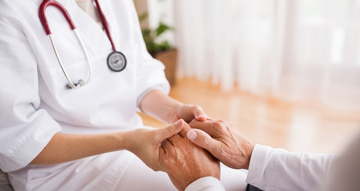 A compassionate nurse with a stethoscope holding a patient's hand.