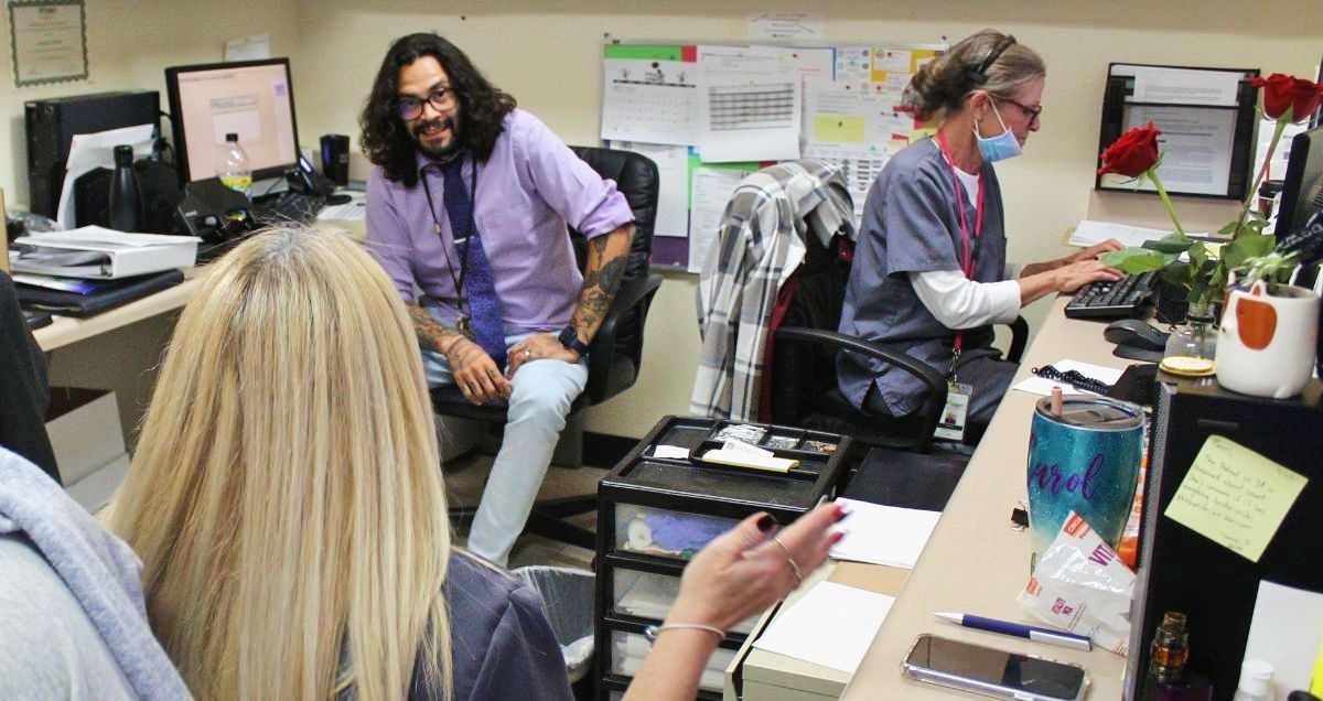 A diverse group of healthcare workers are talking to each other sitting at their desks.