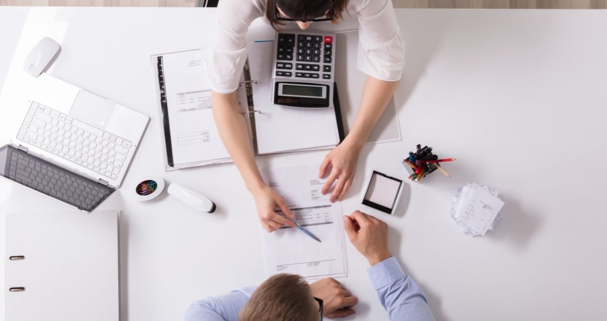 Professional people at a desk with calculators and a computer discussing a document.