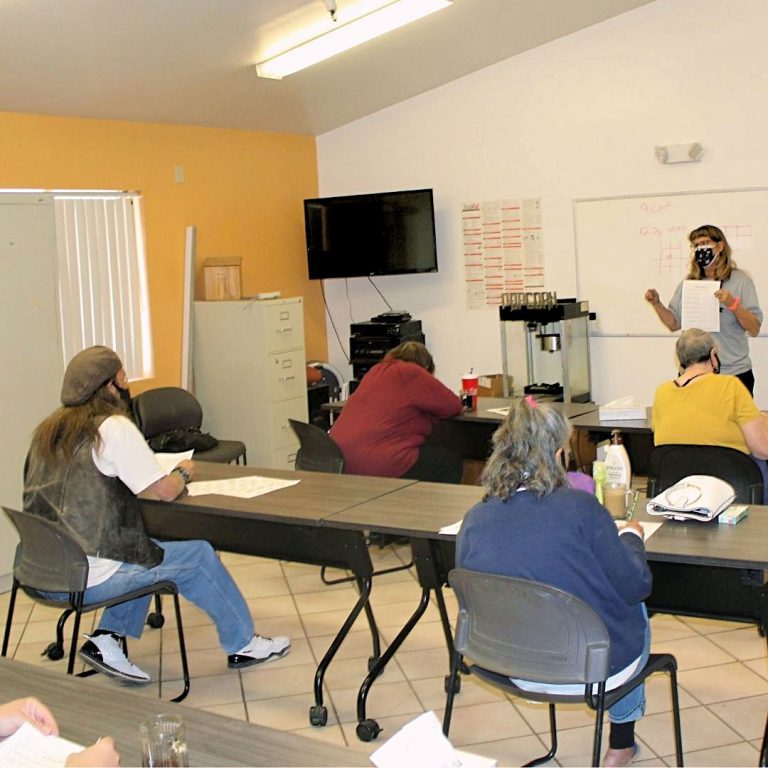 A female teacher holding a paper in front of her class of adult students.