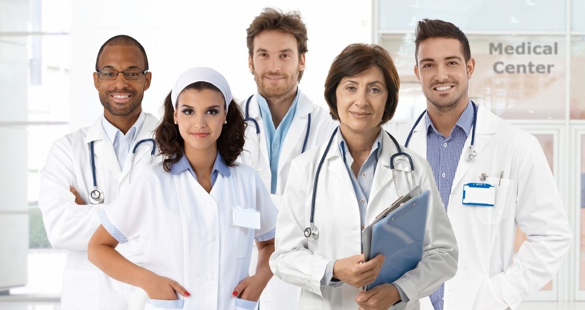 A diverse group of professional doctors and nurses in lab coats smiling with stethoscopes and clipboards.