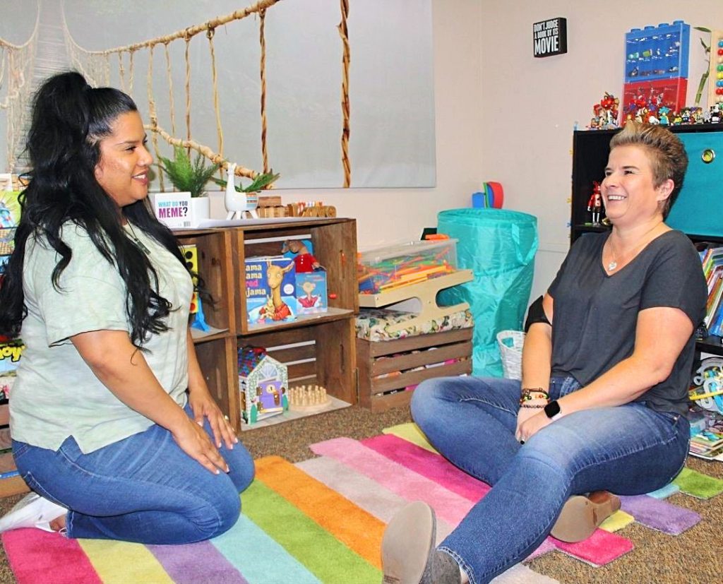 Laughing female Case Managers sitting on the floor in a children's play area surrounded by toys.