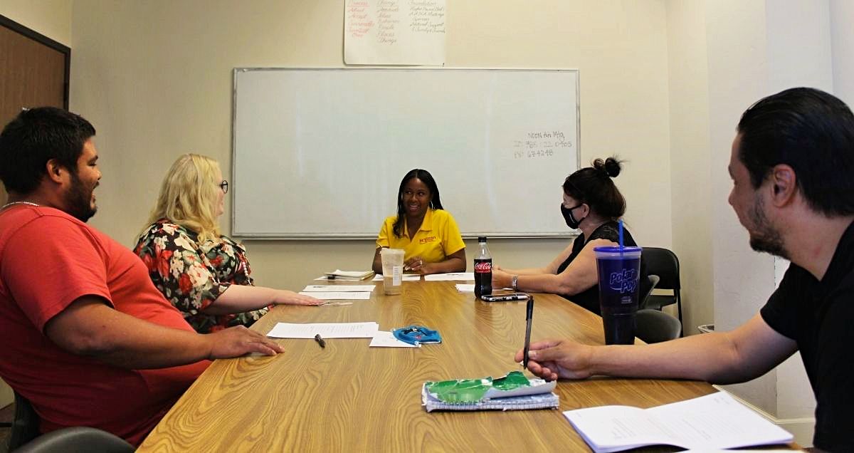 A substance abuse group therapy meeting with a female counselor in a conference room.