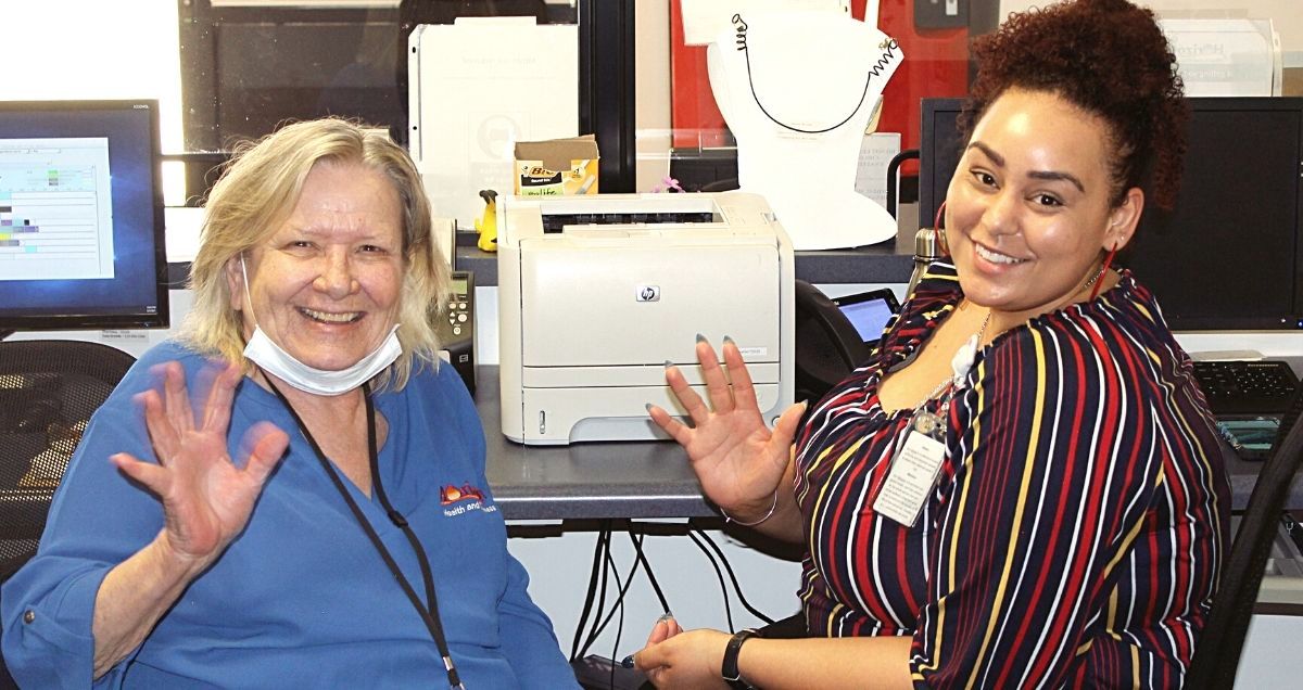 Two smiling Horizon Health and Wellness co-workers sitting at their desks and waving at the camera.