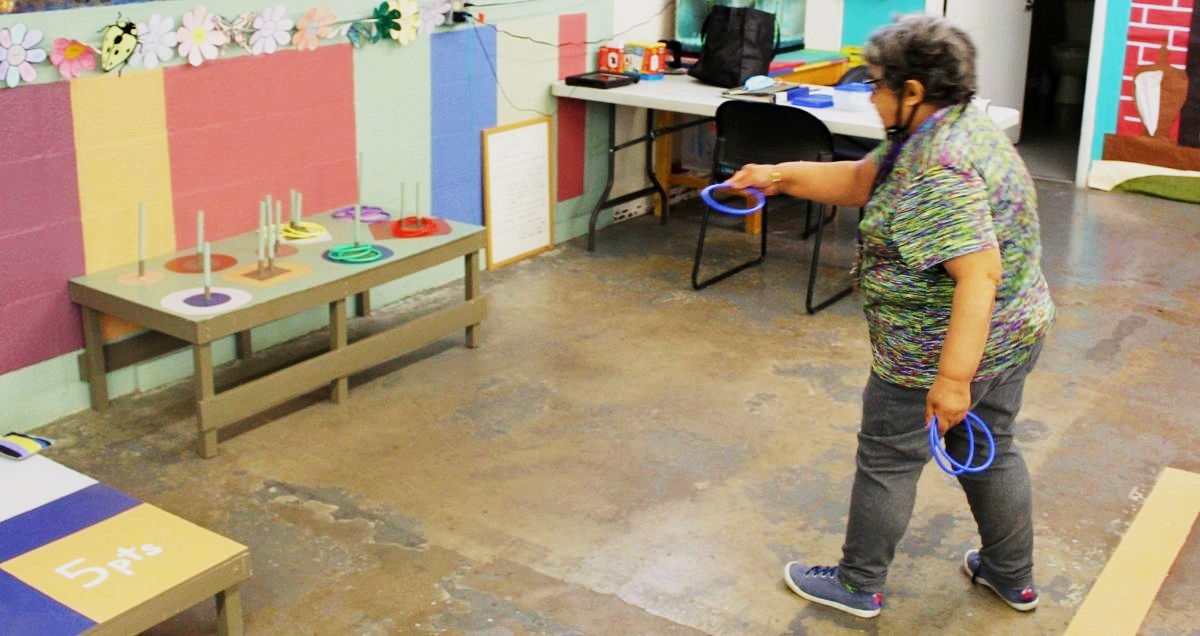 A disabled woman throwing a blue ring in a ringtoss game surrounded by a colorful room.