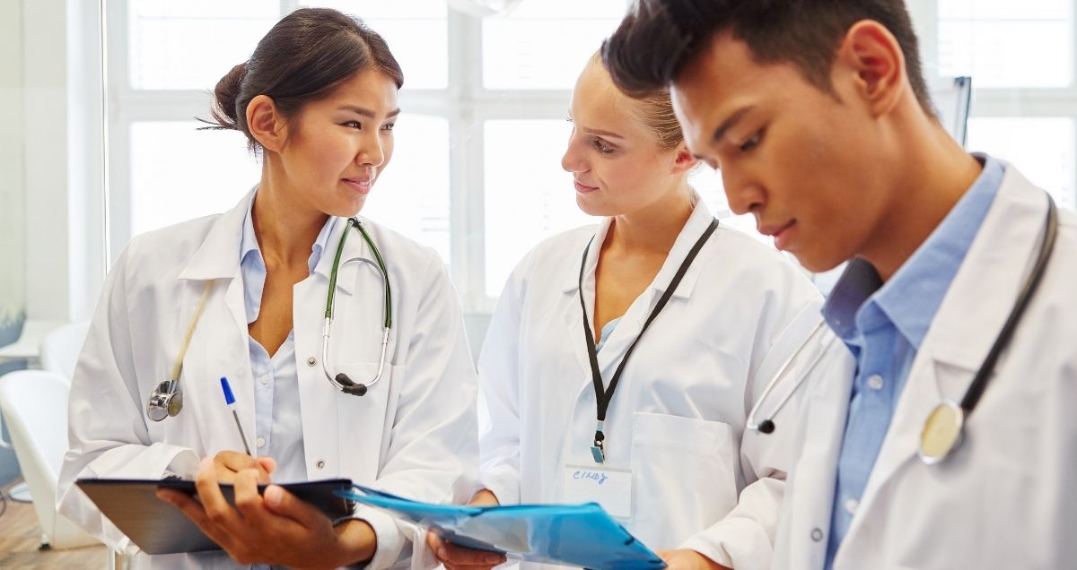 Smiling doctors with stethoscopes and clipboards looking at each other.